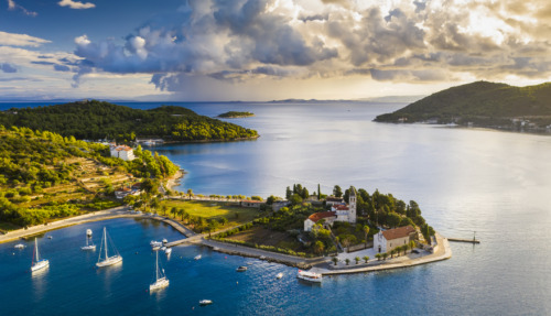 Luchtfoto van het idyllische eiland Vis in Kroatië, omringd door helderblauw water, zeilboten en weelderige natuur.
