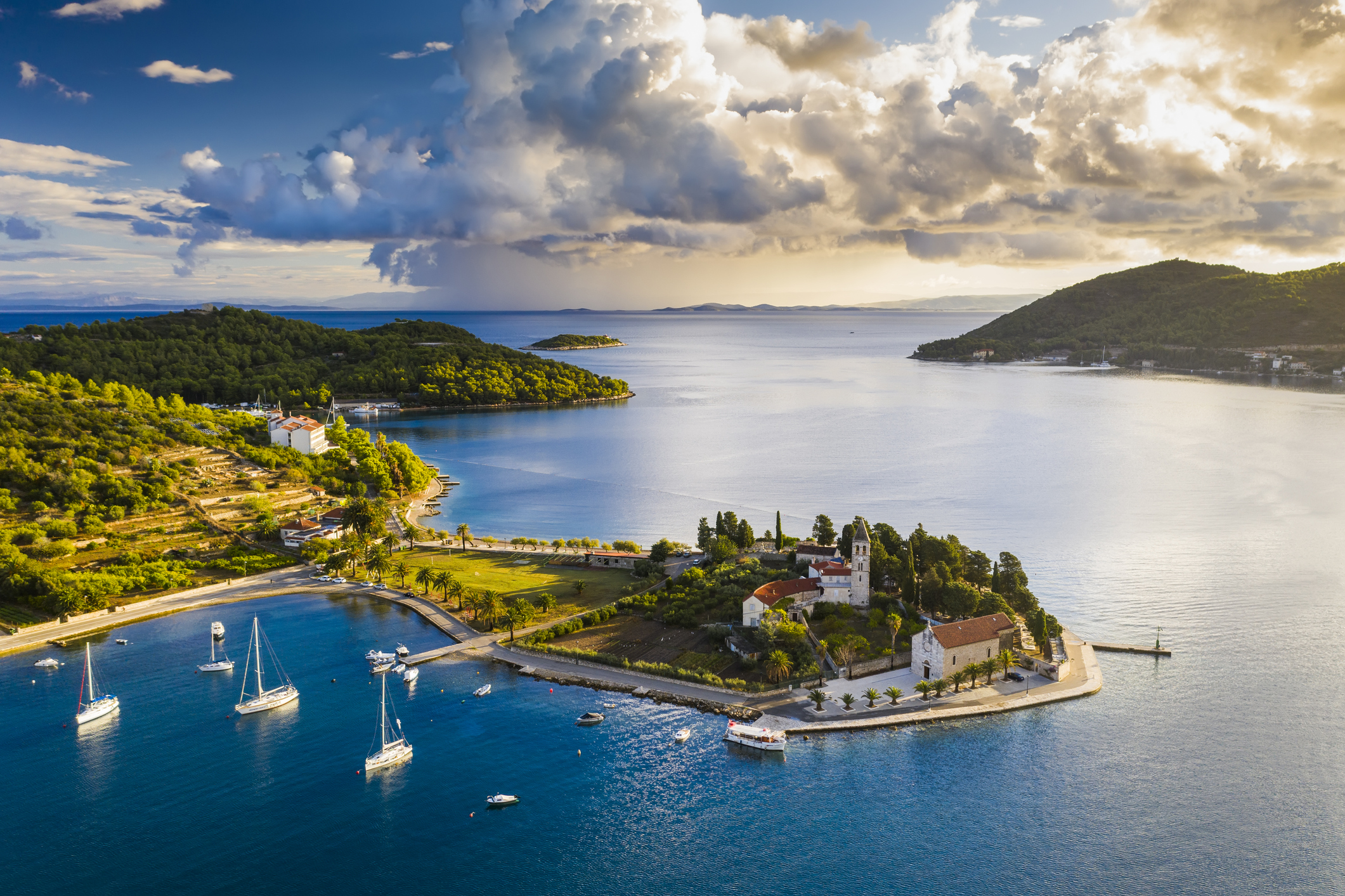 Luchtfoto van het idyllische eiland Vis in Kroatië, omringd door helderblauw water, zeilboten en weelderige natuur.