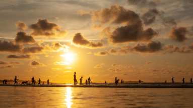 Silhouetten van spelende kinderen aan het strand van Gambia tijdens een kleurrijke zonsondergang.