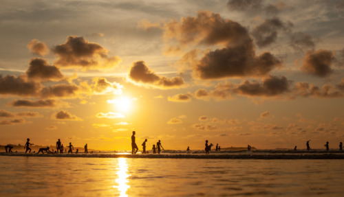 Silhouetten van spelende kinderen aan het strand van Gambia tijdens een kleurrijke zonsondergang.