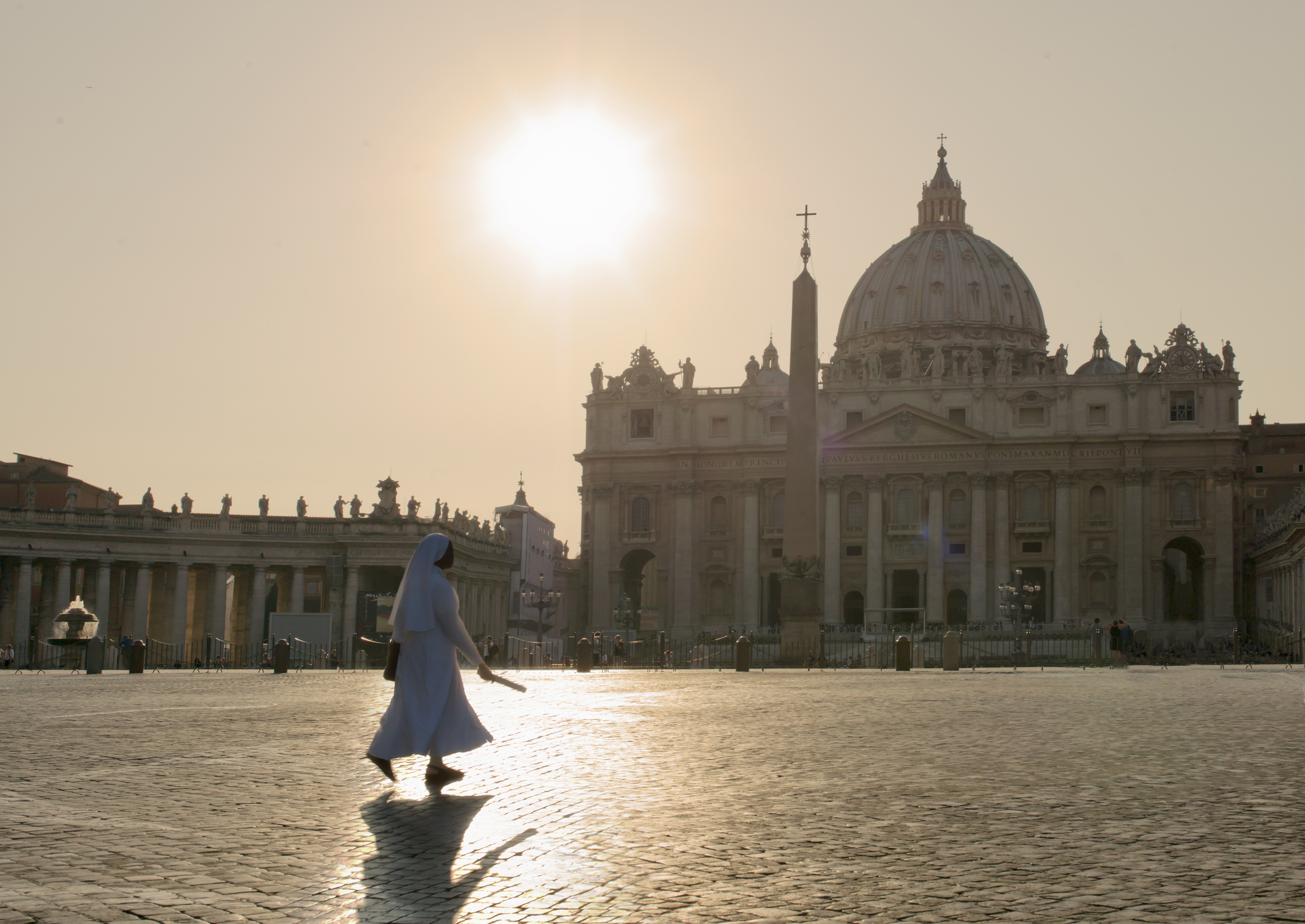 Non wandelend over het Sint-Pietersplein in Vaticaanstad bij zonsopgang, met de iconische Sint-Pietersbasiliek op de achtergrond.