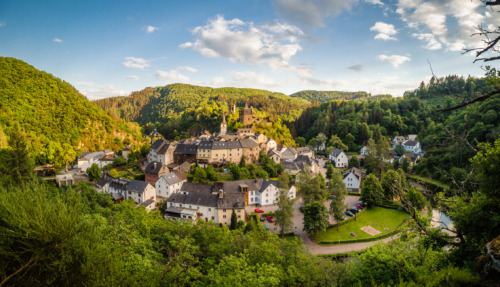 Uitzicht op het pittoreske dorp Esch-Sur-Sur in Luxemburg met groene heuvels, historische gebouwen en een kasteel in een serene omgeving.