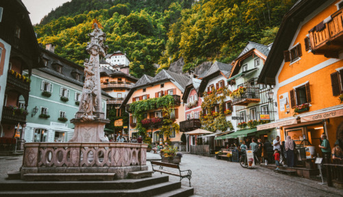 Het pittoreske dorpsplein van Hallstatt in Oostenrijk, omgeven door kleurrijke huizen en weelderige groene bergen.