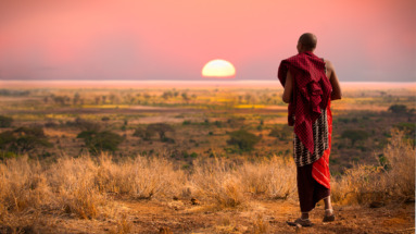 Een Maasai-krijger kijkt uit over de savanne van Tanzania tijdens een adembenemende zonsondergang.