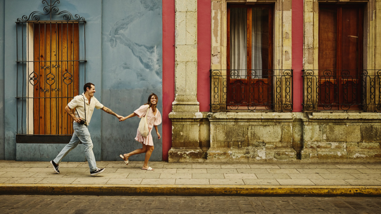 Man en vrouw rennen door de kleurrijke straten van Oaxaca, Mexico