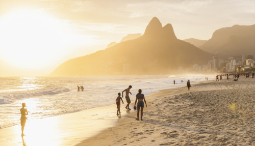 Strandwandeling en spelende kinderen tijdens zonsondergang op Ipanema Beach met de bergen van Rio de Janeiro op de achtergrond