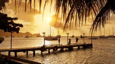 Silhouetten van mensen op een steiger met zeilboten en een gouden zonsondergang op Bequia Island, Port Elizabeth in Saint Vincent en de Grenadines.