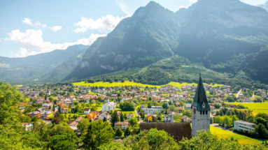 Zicht op het schilderachtige dorp Balzers in Liechtenstein met groene heuvels, imposante bergen en een historische kerk.