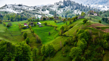 Groene heuvels en besneeuwde bergen in de Karpaten, Roemenië, met traditionele boerderijen en landelijke charme.