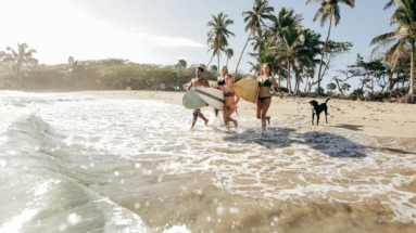 Een groep jonge surfers rent met hun surfplanken de oceaan in op een tropisch strand in de Dominicaanse Republiek.