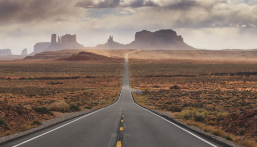 Eindeloze weg door het woestijnlandschap van Monument Valley in de Verenigde Staten, met roodgekleurde rotsformaties op de achtergrond.