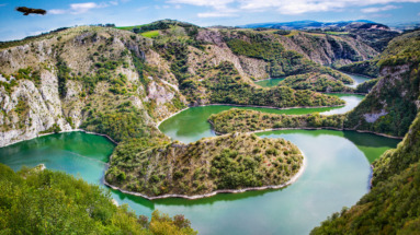 Een luchtfoto van de kronkelende Uvac-rivier omringd door groene heuvels in Servië, een verborgen parel in de Balkan met indrukwekkende natuur en eeuwenoude geschiedenis.
