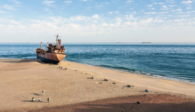 Een roestig scheepswrak op het zandstrand aan de kust van Mauritanië bij Nouadhibou, met een diepblauwe zee en een heldere lucht op de achtergrond.