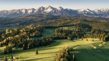 Uitzicht over de Tatra-gebergte en omliggende groene valleien in Polen bij zonsopgang, met helderblauwe lucht en rustige landschappen.