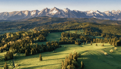 Uitzicht over de Tatra-gebergte en omliggende groene valleien in Polen bij zonsopgang, met helderblauwe lucht en rustige landschappen.