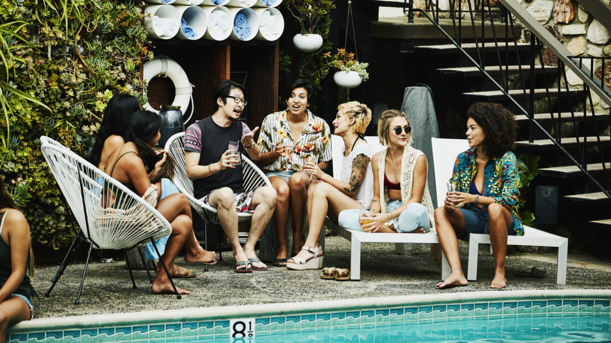 Groep jonge reizigers in gesprek bij een zwembad, genietend van een ontspannen sfeer.