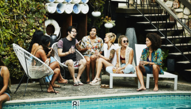 Groep jonge reizigers in gesprek bij een zwembad, genietend van een ontspannen sfeer.