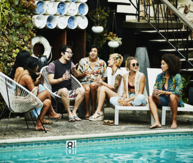 Groep jonge reizigers in gesprek bij een zwembad, genietend van een ontspannen sfeer.