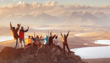 Groep reizigers viert samen een overwinning op een bergtop bij zonsondergang.