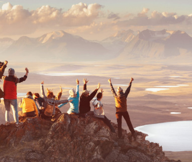 Groep reizigers viert samen een overwinning op een bergtop bij zonsondergang.
