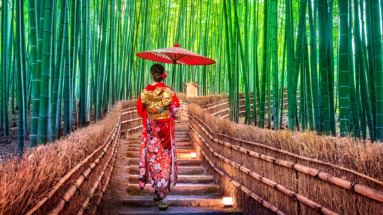 Een vrouw in een traditionele kimono loopt met een rode parasol door het bamboebos van Arashiyama in Kyoto, Japan.