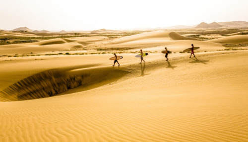 Surfers lopen door de zandduinen Ash Sharquiyah in Oman, een land vol woestijnlandschappen en avontuur.