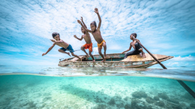 Bajau Kinderen springen van een traditionele boot in het heldere water bij de kust van Maleisië, omringd door een tropisch paradijs.