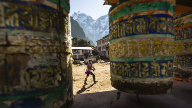 Een trekker loopt langs gebedsmolens bij de Tengboche Monastery met Himalaya-pieken op de achtergrond in Sagarmatha National Park, Nepal.