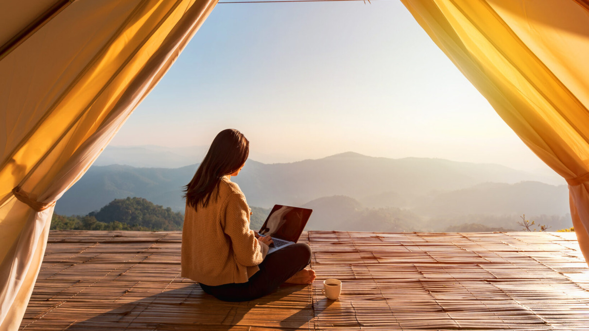 Vrouw met laptop in een tent met uitzicht op de bergen, symbool voor interactief meedoen aan quizzen, webinars en winacties