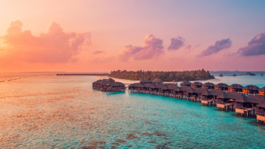 Waterbungalows op de Malediven bij zonsondergang, omgeven door turquoise water en witte zandstranden.
