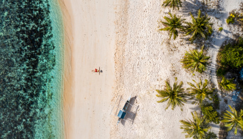 Bounty-strand met palmbomen, wit zand en turquoise water op de Filipijnen, met een ontspannende reiziger onder de zon.
