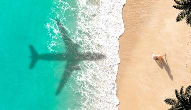 Schaduw van een vliegtuig boven een turquoise zee en een zandstrand
