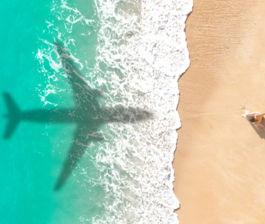 Schaduw van een vliegtuig boven een turquoise zee en een zandstrand