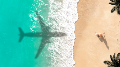 Schaduw van een vliegtuig boven een turquoise zee en een zandstrand
