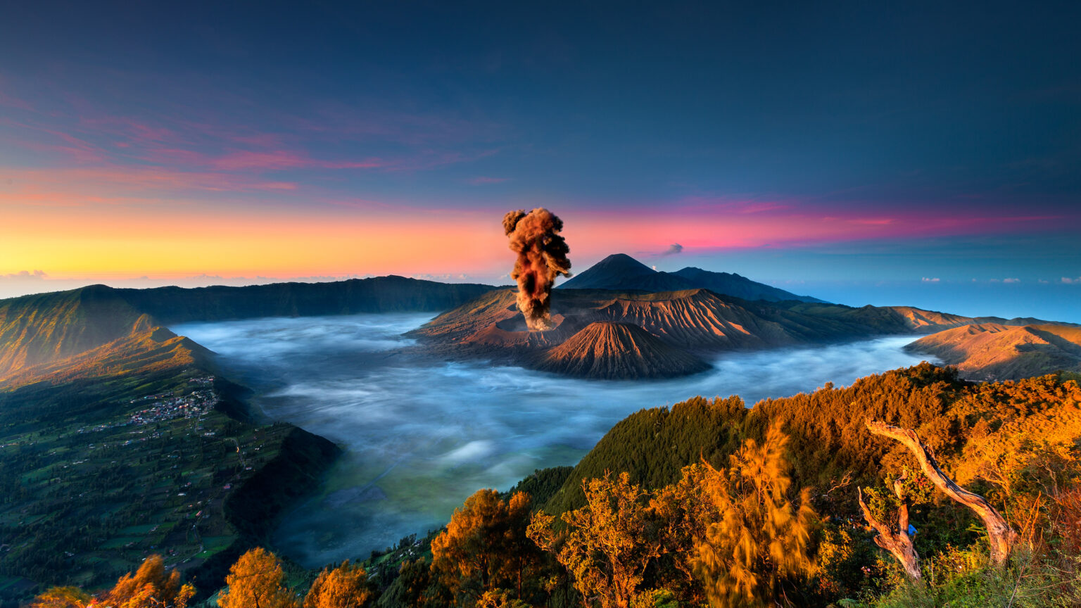De Bromo-vulkaan in Indonesië barst uit bij zonsopgang, omgeven door een mistig berglandschap.