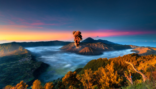 De Bromo-vulkaan in Indonesië barst uit bij zonsopgang, omgeven door een mistig berglandschap.