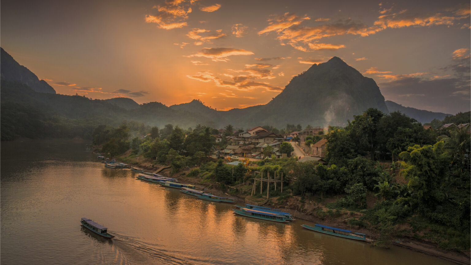 en sfeervol landschap in Laos met een rivier, bergen en een kleurrijke zonsondergang.