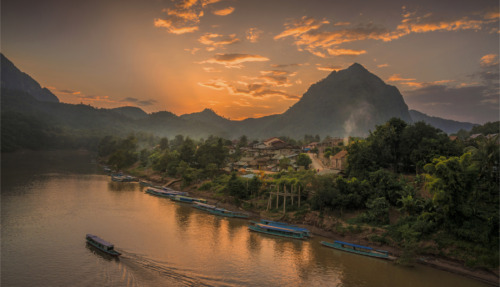 en sfeervol landschap in Laos met een rivier, bergen en een kleurrijke zonsondergang.