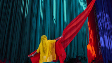 Een Indiase vrouw in een felgele sari hangt rood textiel op tegen een achtergrond van kleurrijke stoffen.