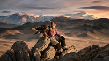 Jonge adelaarjager in traditionele kleding met zijn Altai-adelaar in het bergachtige landschap van Ulgii, Mongolië.