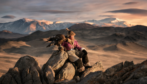 Jonge adelaarjager in traditionele kleding met zijn Altai-adelaar in het bergachtige landschap van Ulgii, Mongolië.