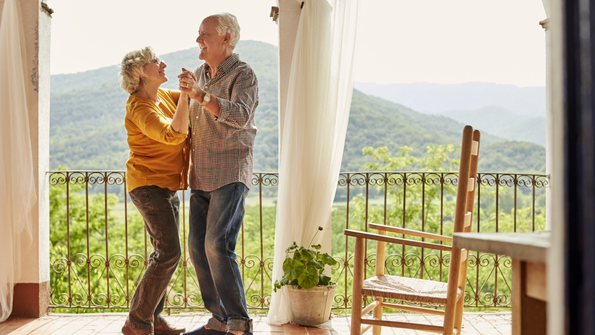 Bejaard koppel danst verliefd en vrolijk op een balkon in de zon