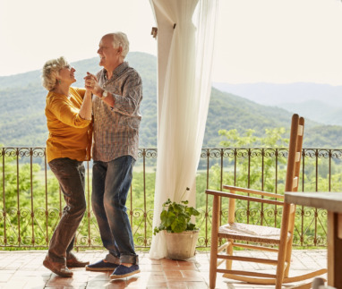 Bejaard koppel danst verliefd en vrolijk op een balkon in de zon