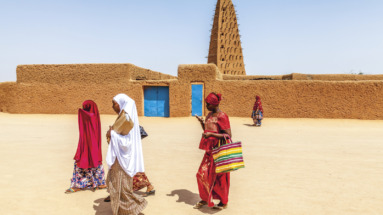 Traditioneel geklede vrouwen lopen langs een historische lemen moskee in Niger.
