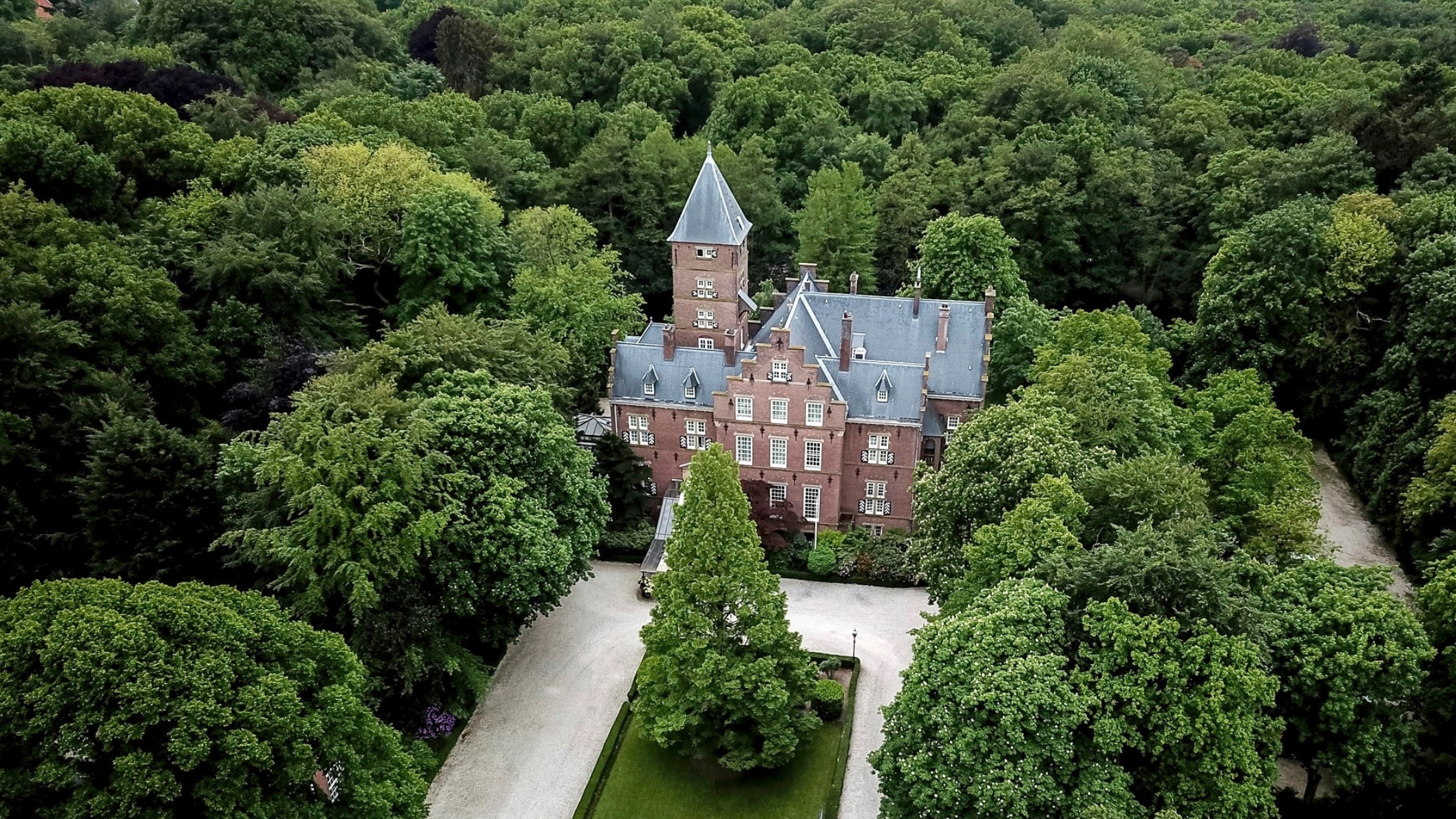 Luchtfoto van Kasteel De Wittenburg, een statig historisch landhuis in Wassenaar, omringd door een weelderig groen bos en een elegante oprijlaan. Foto: Paco van Leeuwen