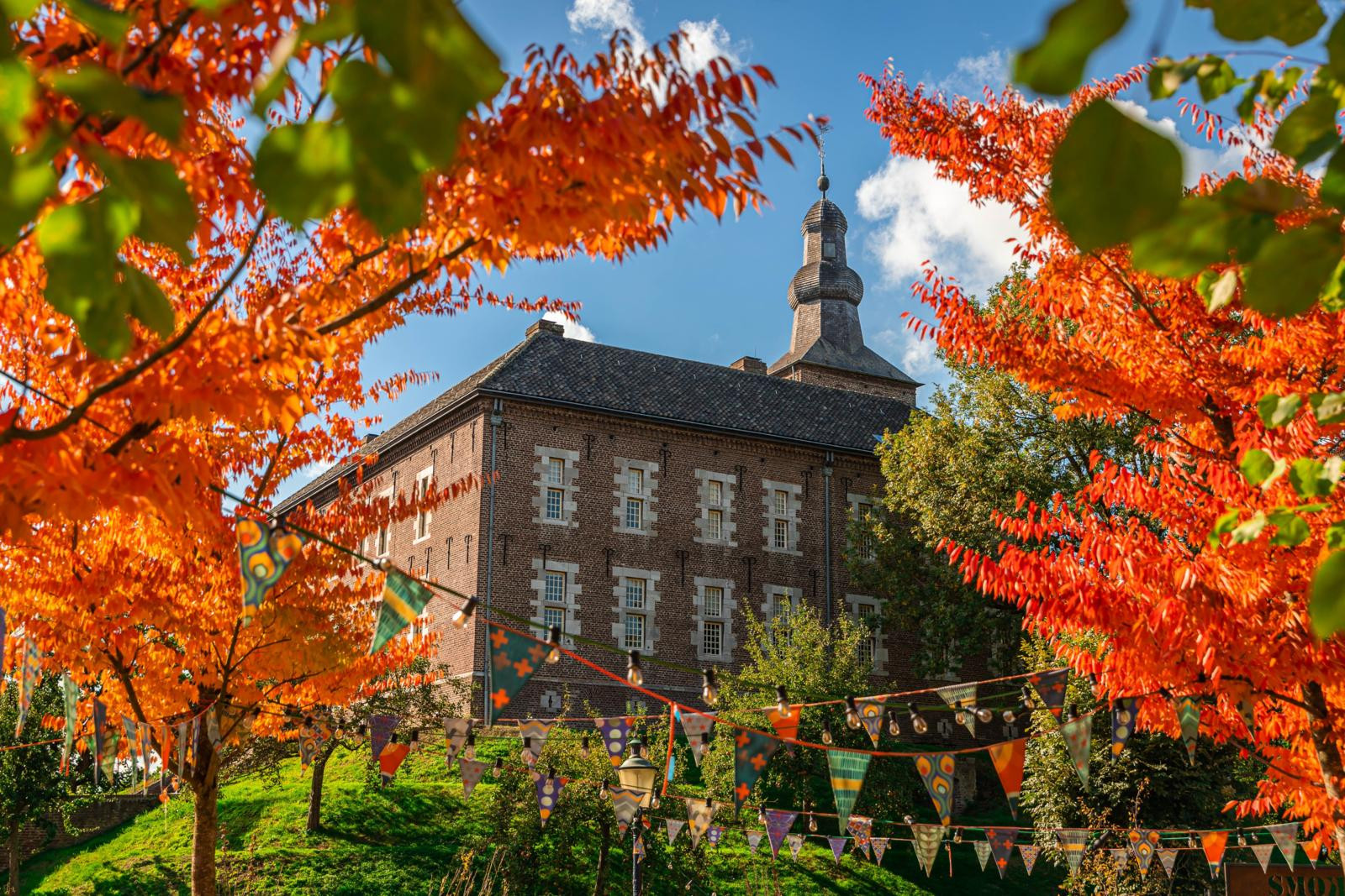 Kasteel Limbricht, een historisch waterkasteel in Limburg, omringd door een gracht en groene natuur, met een levendige binnenplaats en terras. 
