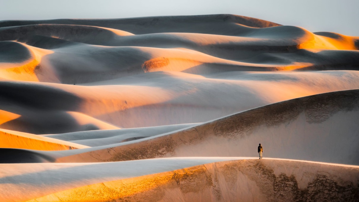 Reiziger op massale zandduinen tijdens zonsondergang