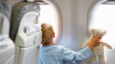 Kind kijkt met knuffel uit het raam van een vliegtuig tijdens een vlucht