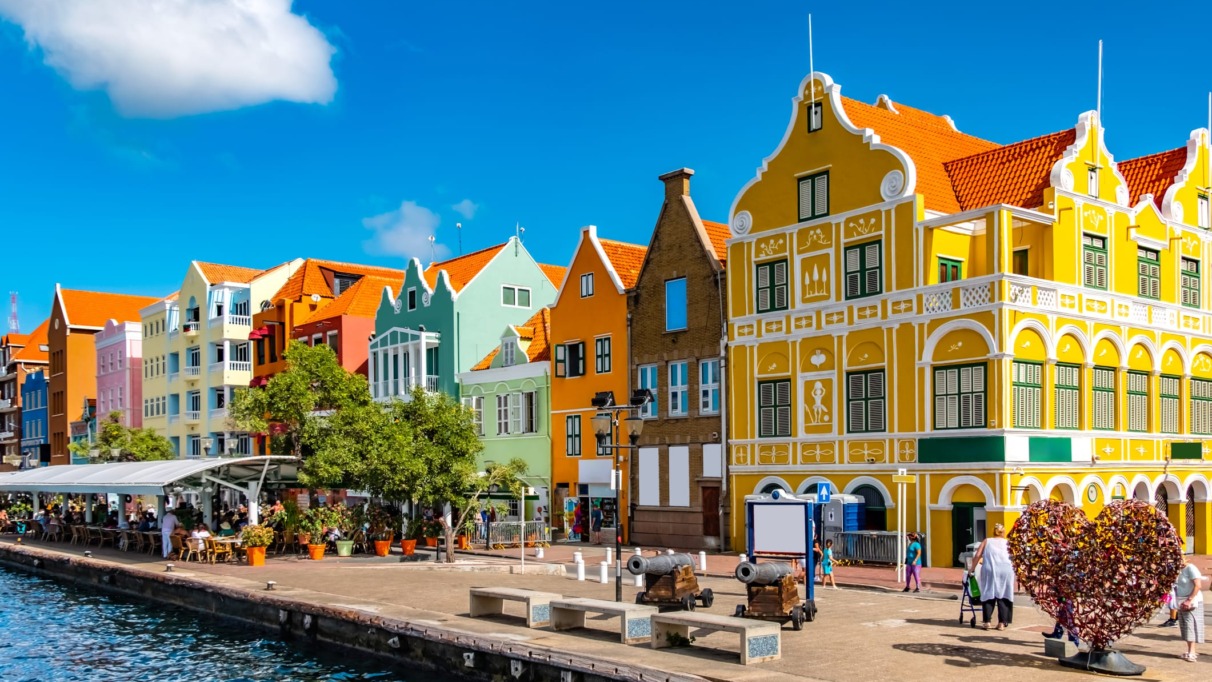 Historische gekleurde gevels aan de waterkant van Willemstad, Curaçao, met terrassen en een helderblauwe lucht
