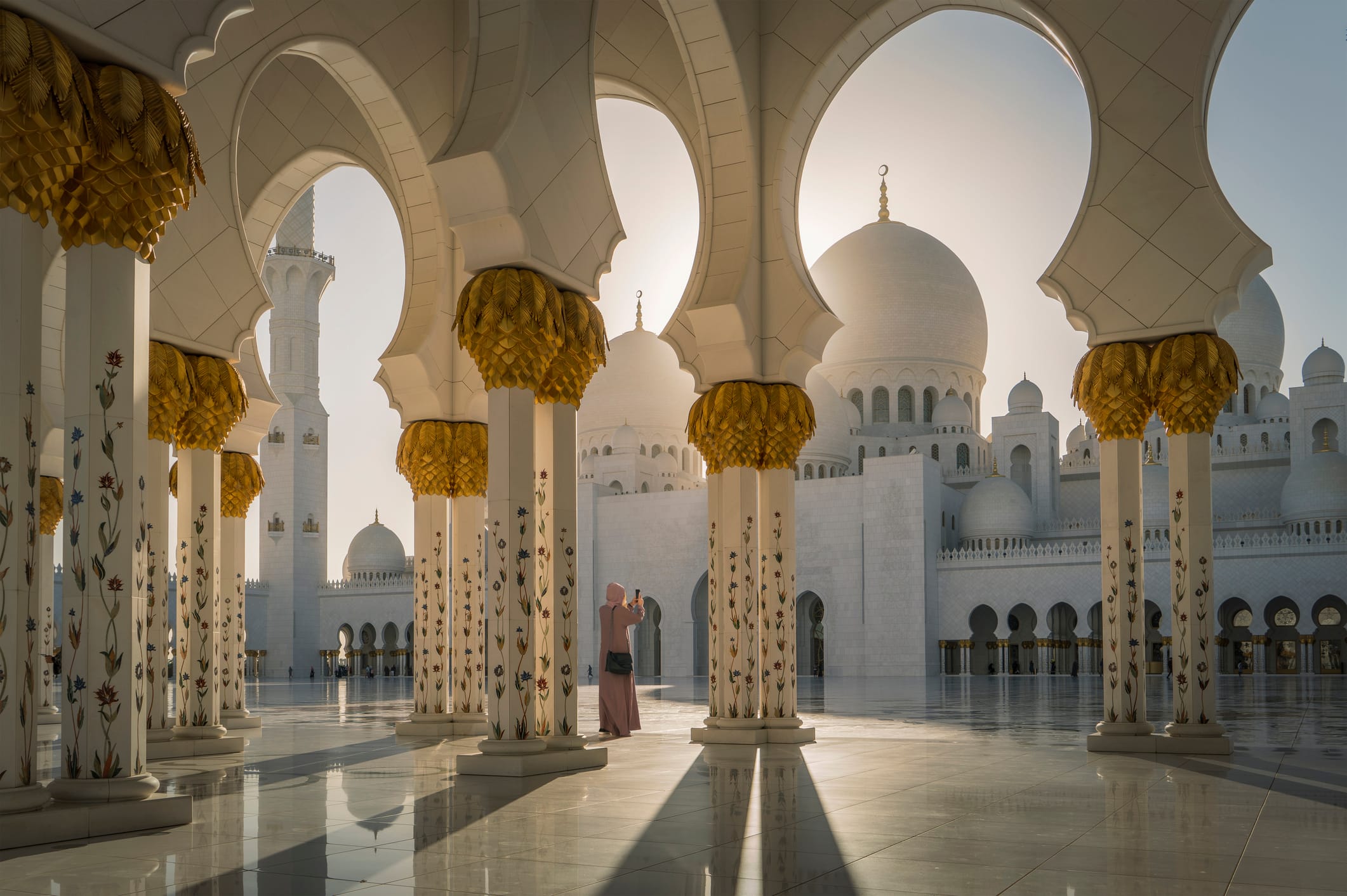 Vrouw in traditionele kleding bezoekt de Sheikh Zayed-moskee in Abu Dhabi bij zonsopkomst